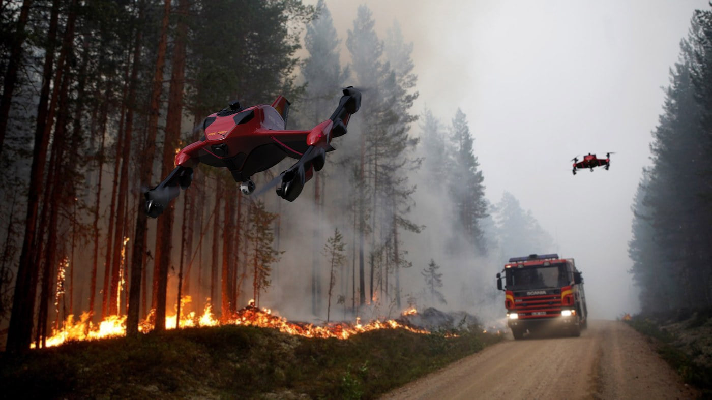 A red Recruit drone flying above a wildfire scene with a fire truck on a forest road.
