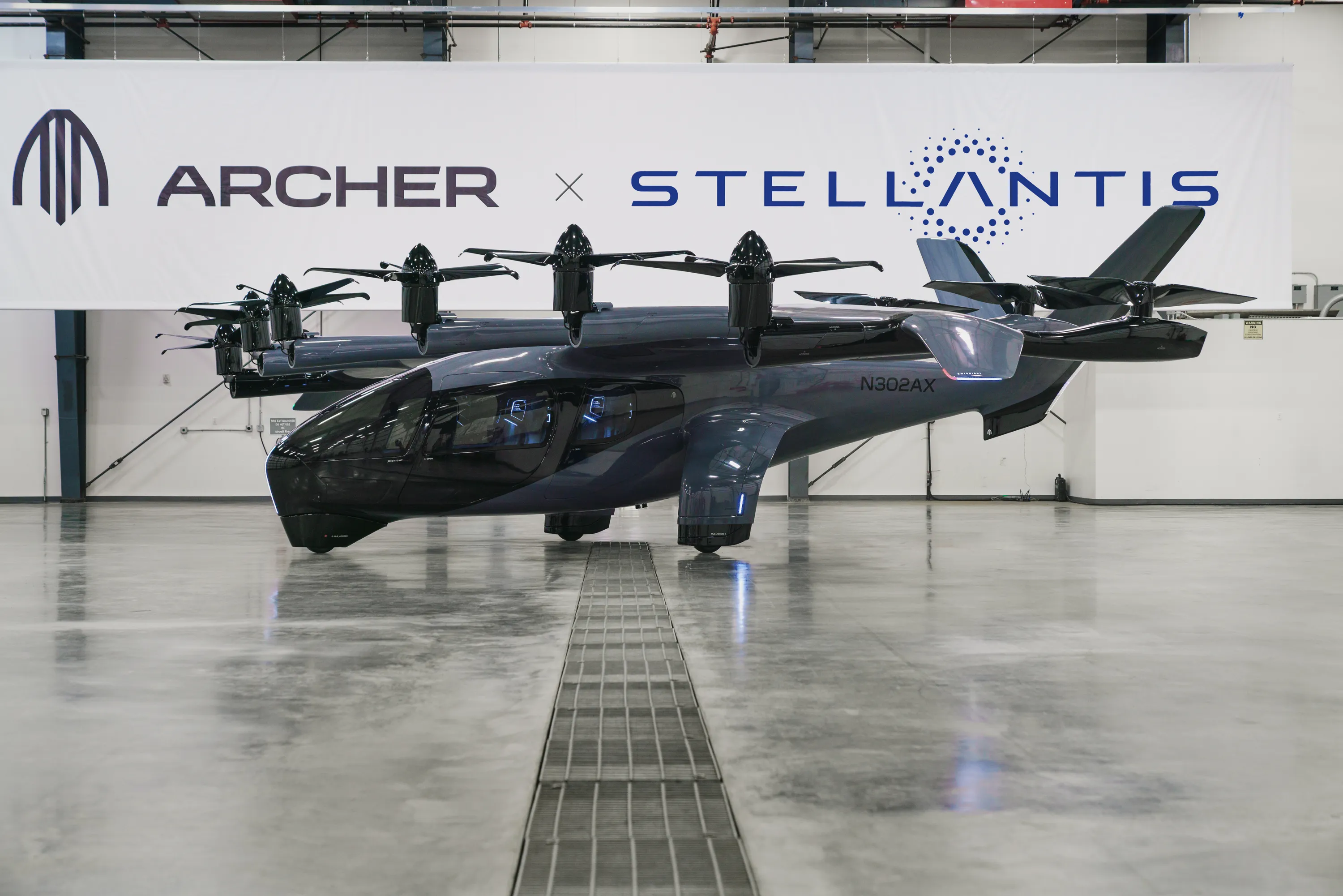 Archer Aviation Midnight eVTOL aircraft on display in a hangar with the Archer x Stellantis banner behind it.