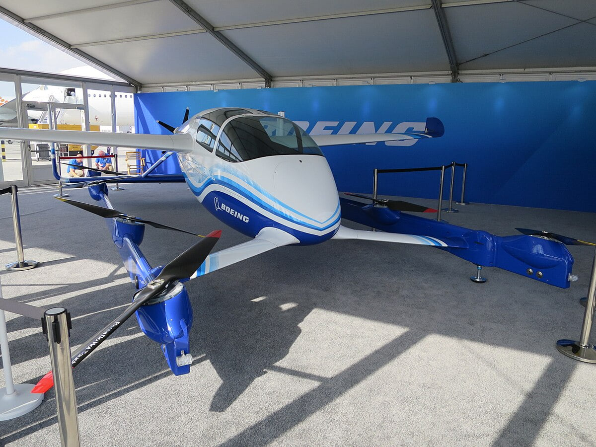 A small Boeing eVTOL passenger air taxi prototype on display, with white and blue livery.